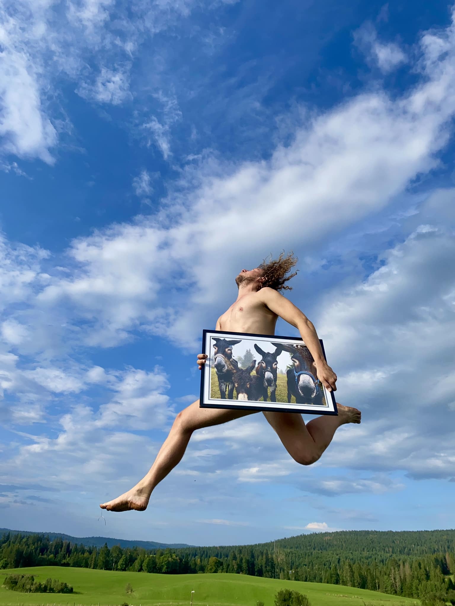 un ciel bleu avec quelques nuages et un champ vert. un homme saute nu, portant une photo