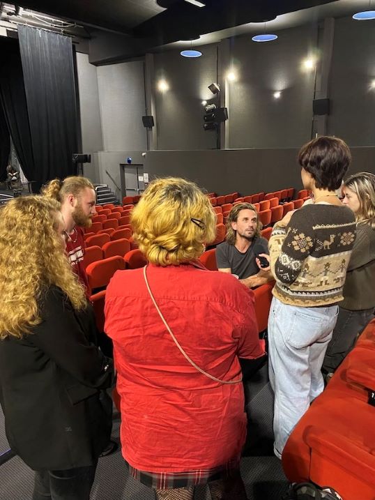 Dans une salle de spectacle, plusieurs adolescents interviewent, micro en main, un comédien.