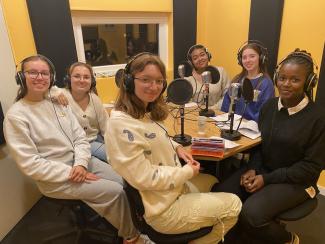 Un groupe de jeunes filles nous regarde en souriant, installé dans un studio d'enregistrement radio.